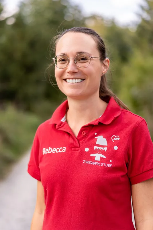 Frau, rotes Shirt, lange braune Haare als Zopf, Brille, lächelt